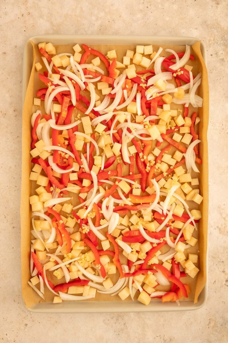 Peppers, potatoes and onions on a parchment lined sheet pan.