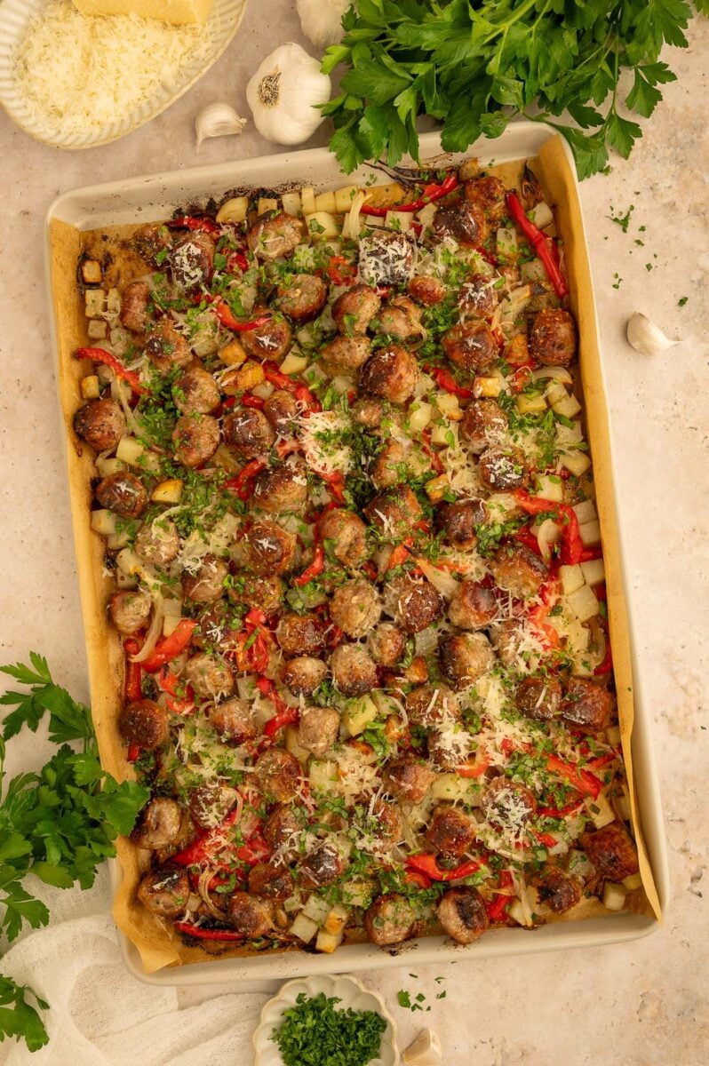 Sausage, peppers, potatoes, and onions on a sheet pan with fresh ingredients on the side.