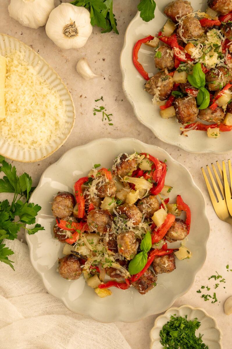 An overhead shot of sausage, peppers, potatoes, and onions on two plates with more ingredients on the side.