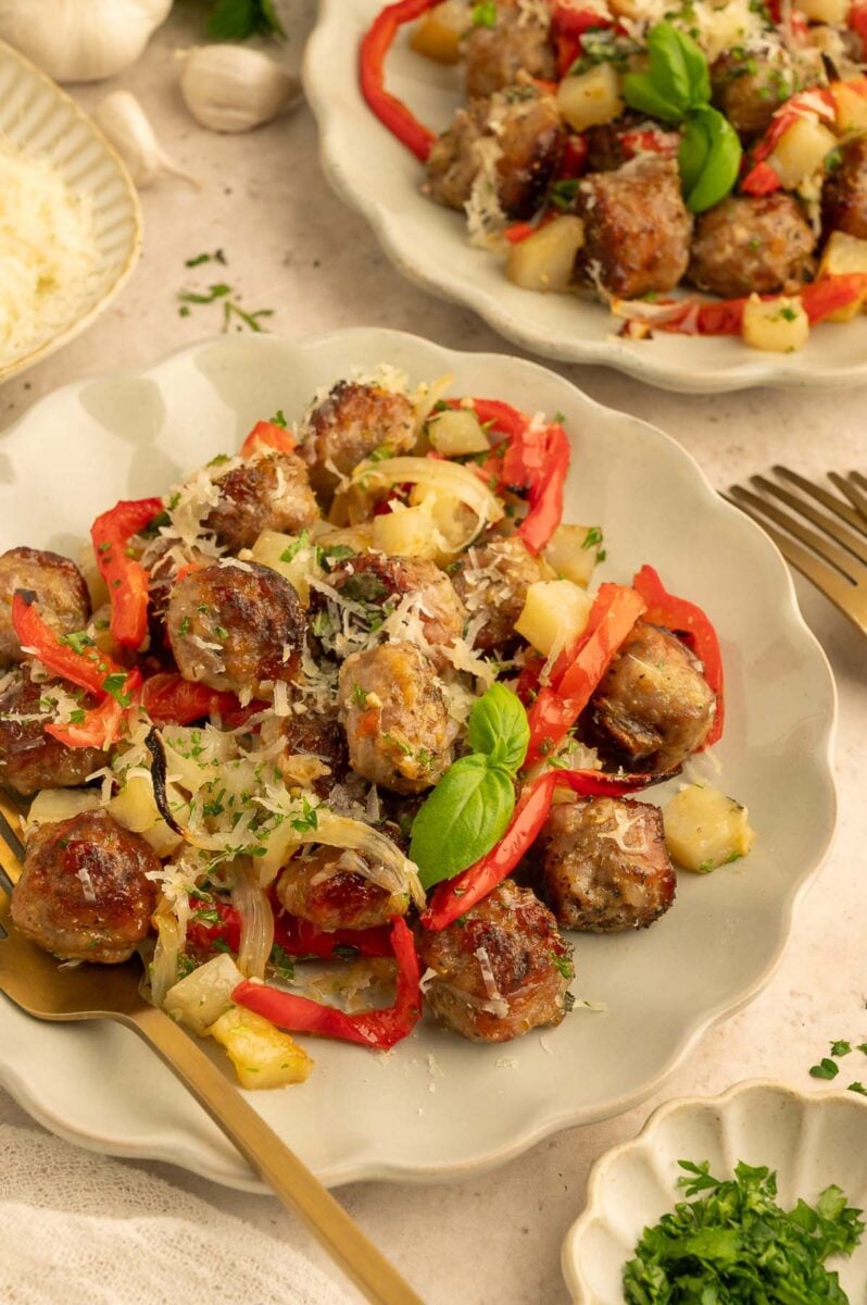 A plate of sausage, peppers, potatoes, and onions with a fork resting on the plate and another plate in the background.