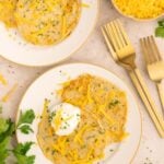 Savory pancakes on a white plate topped with cheddar cheese and fresh herbs.
