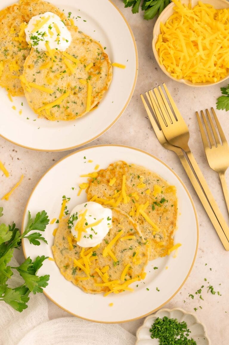 Savory pancakes on a white plate topped with cheddar cheese and fresh herbs.