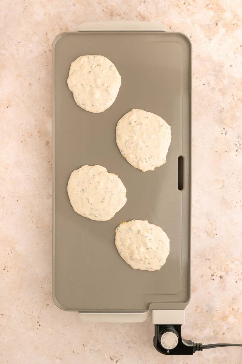 Four uncooked cheddar savory pancakes cooking on a griddle. 