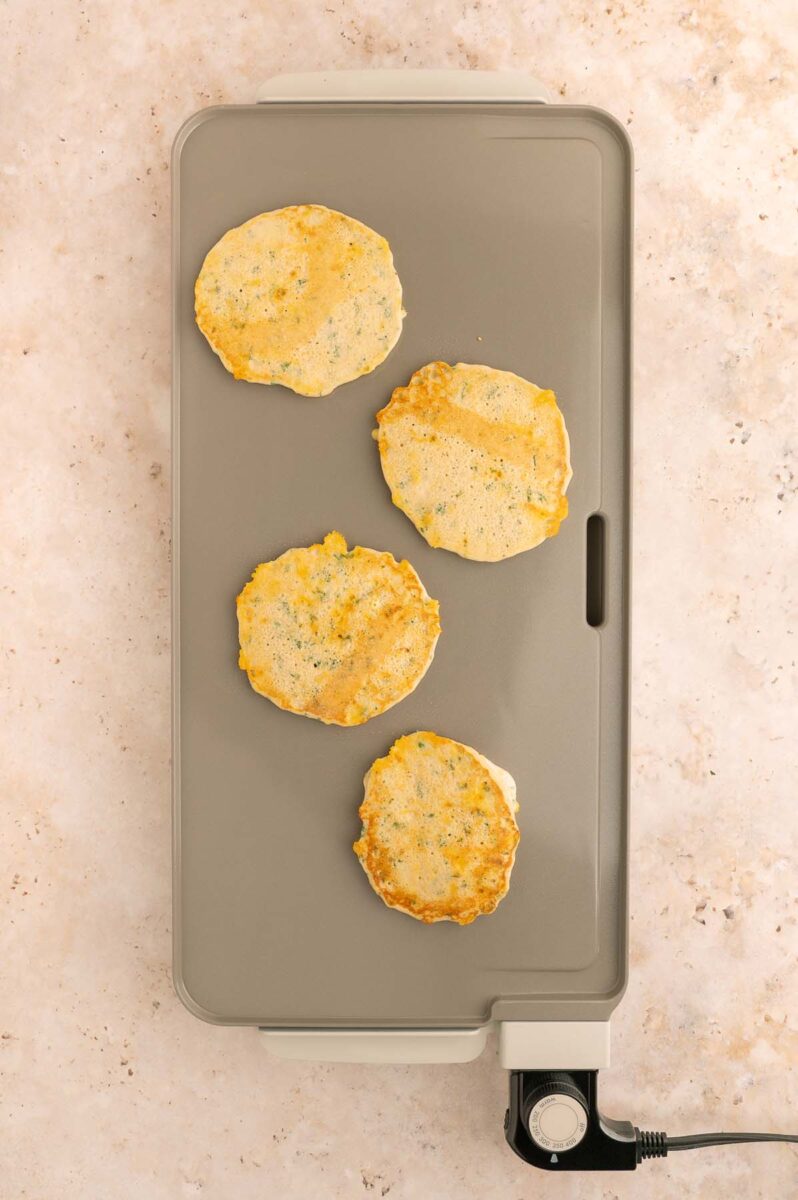 Four savory pancakes cooking on a griddle.