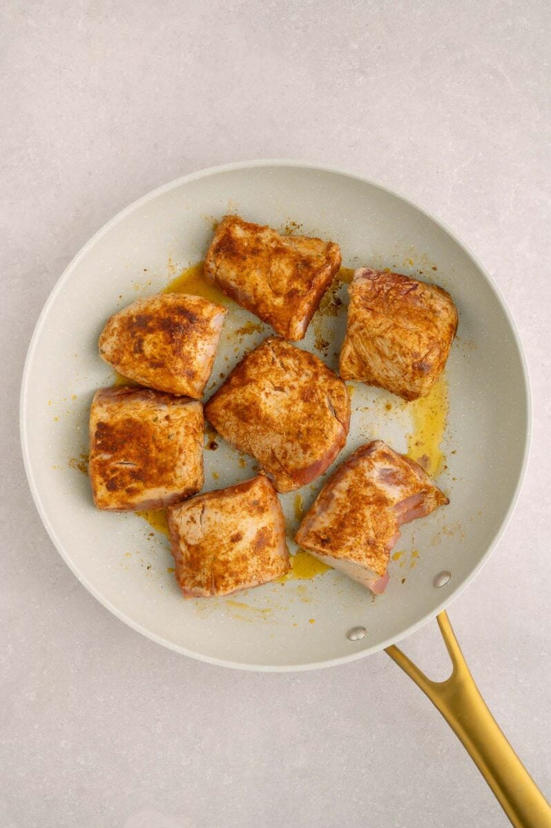 Seasoned pork tenderloin pieces in a pan after cooking until golden brown.