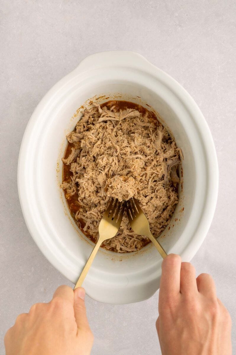 Two forks shredding pork in a crockpot base. 