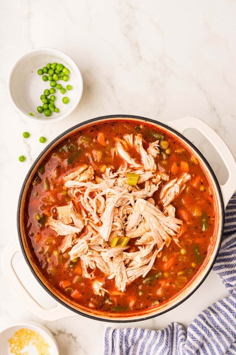 A pot of alphabet soup with shredded chicken on top before stirring in. 