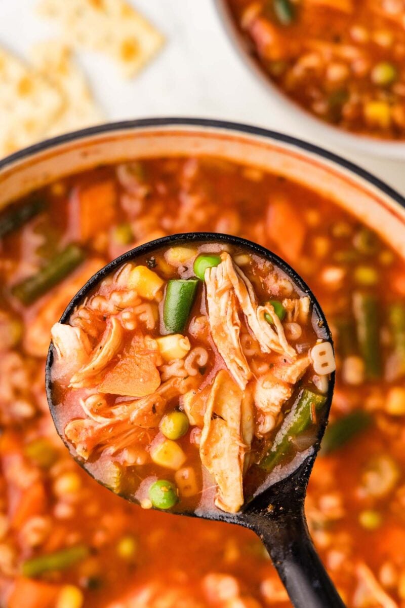 A large ladle of soup being scooped out of a pot of alphabet soup.