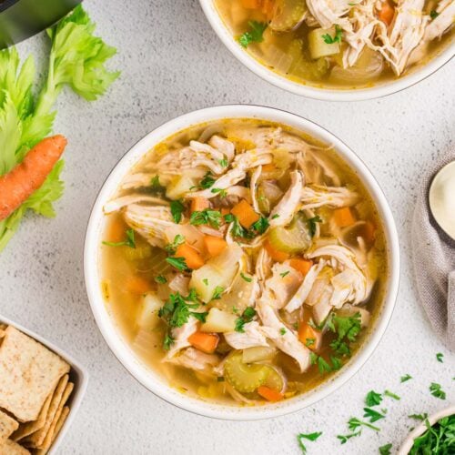 Chicken Potato Soup in two white bowls on a counter with ingredients on the side.