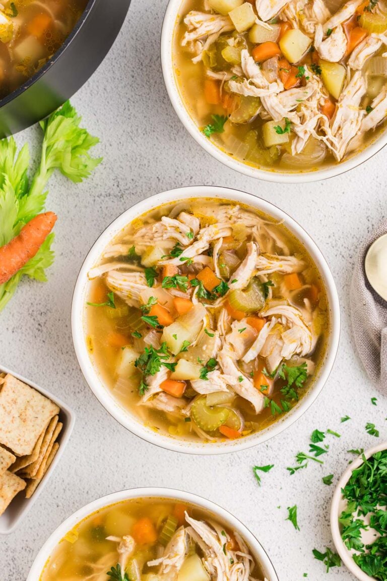 Chicken Potato Soup in two white bowls on a counter with ingredients on the side.