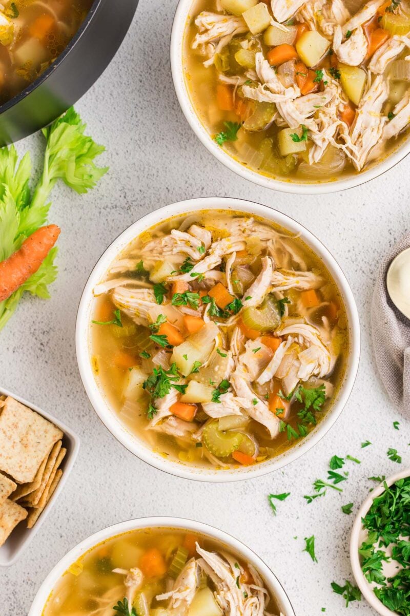 Chicken Potato Soup in two white bowls on a counter with ingredients on the side.