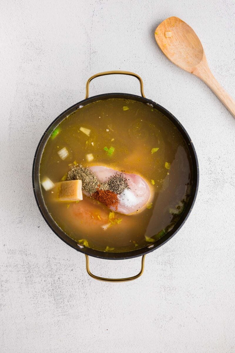 Ingredients for chicken potato soup in a large pot before cooking and mixing together with a wooden spoon beside it. 