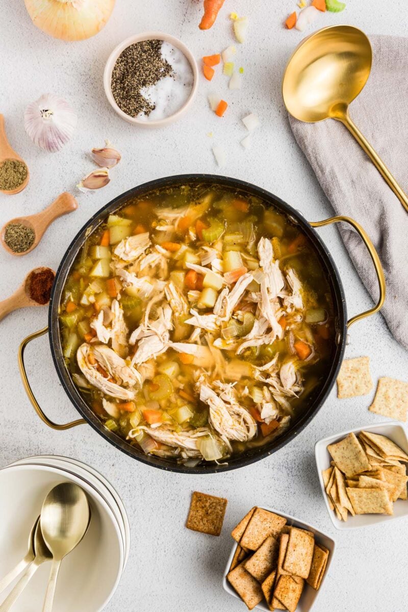 Chicken potato soup in a large pot with ingredients and a golden ladle on the side.