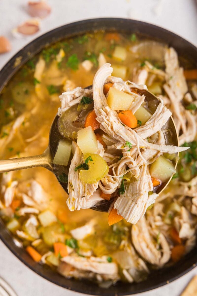 A ladle taking a large scoop of chicken potato soup out of a pot of the soup.