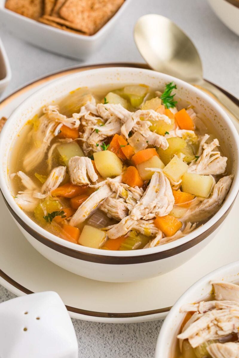 A white bowl of chicken potato soup with a soup in the background.