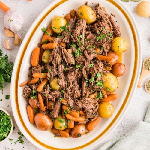 Dutch Oven Pot Roast with carrots and potatoes on a white platter with ingredients on the side.