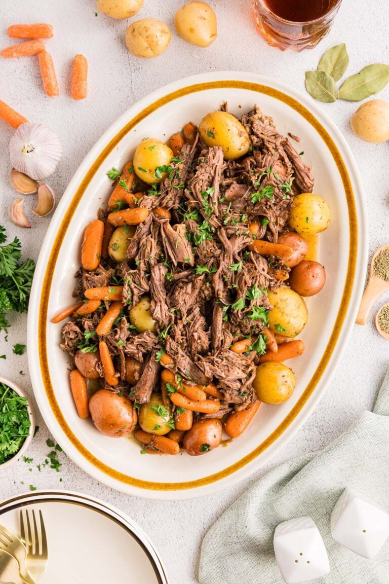 Dutch Oven Pot Roast with carrots and potatoes on a white platter with ingredients on the side.