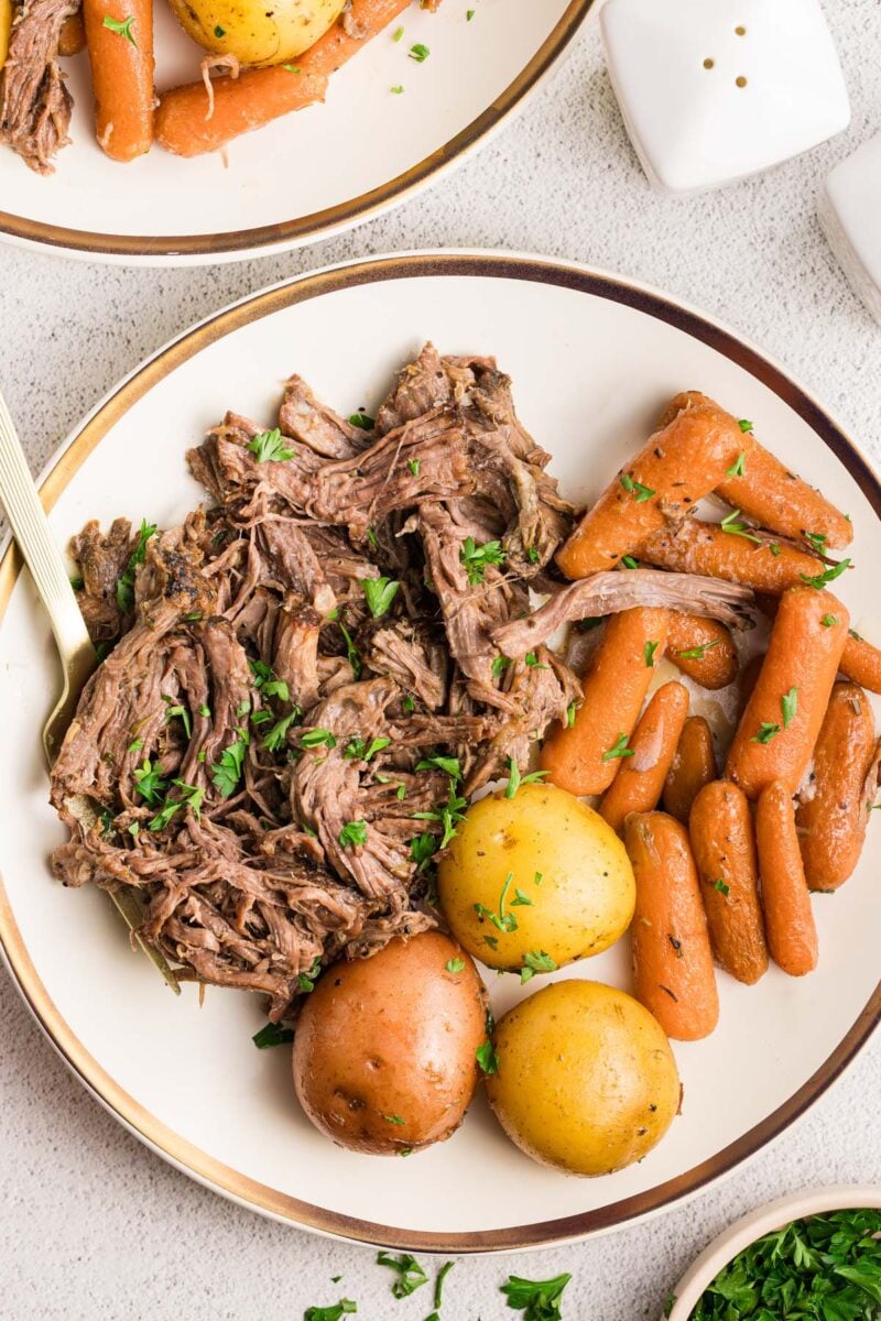 Shredded Pot Roast, Carrots, and Potatoes on a white plate with a fork in the roast.