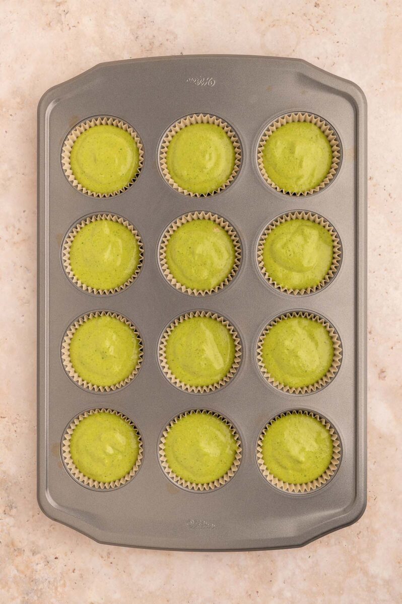 Green muffin batter in a lined muffin pan before baking.