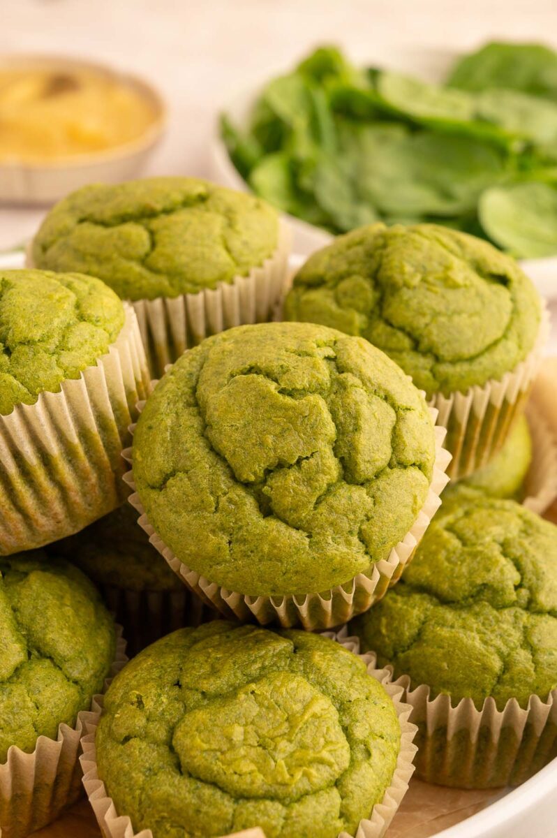 Green Muffins in a pile on a plate with spinach in the background.
