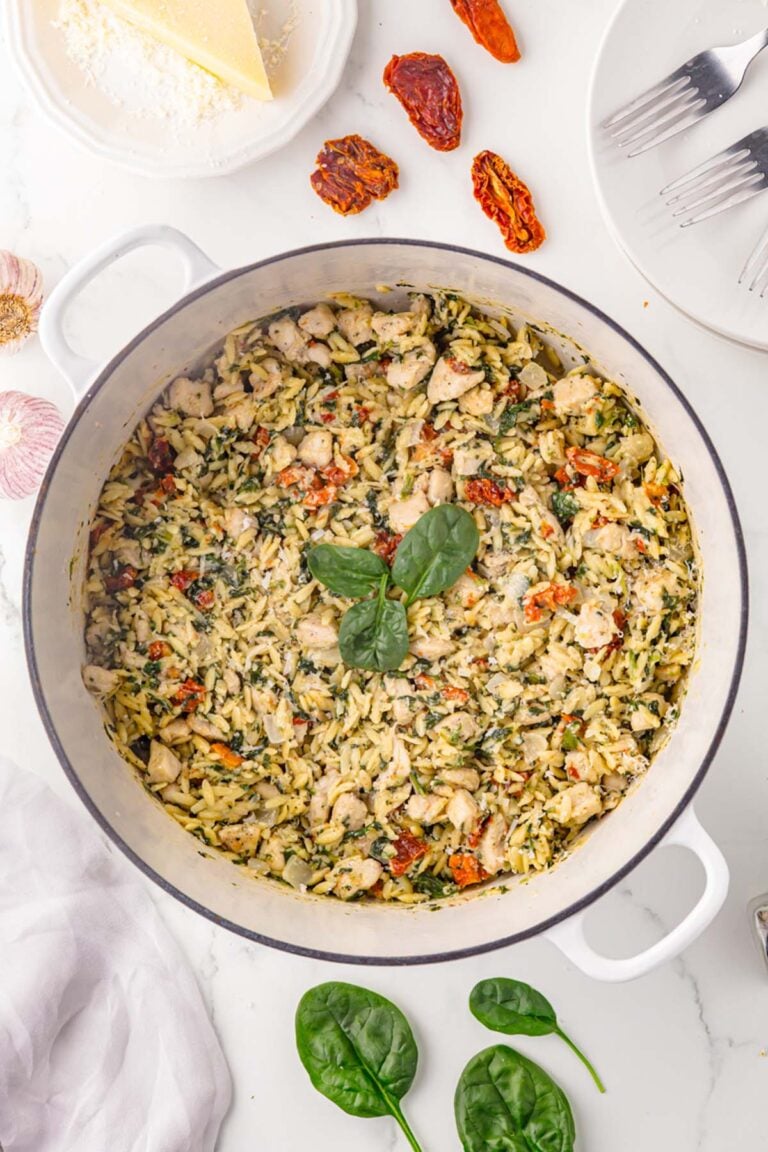 Tuscan Chicken Orzo in a dutch oven with spinach and sun dried tomatoes on the side.