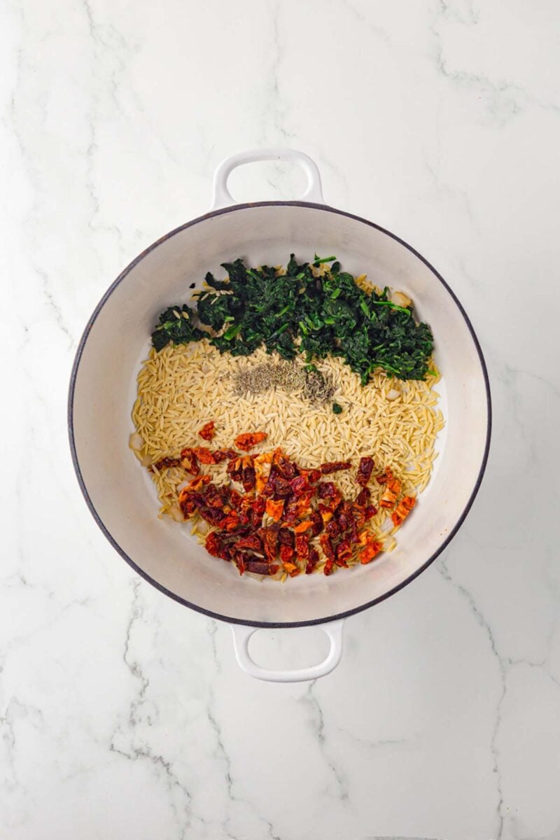Orzo, spinach, sun dried tomatoes, and spices added to onions and garlic in a dutch oven.