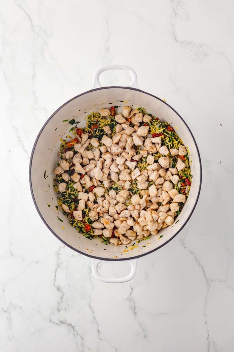 Tuscan chicken orzo in a dutch oven before mixing together and fully cooking.