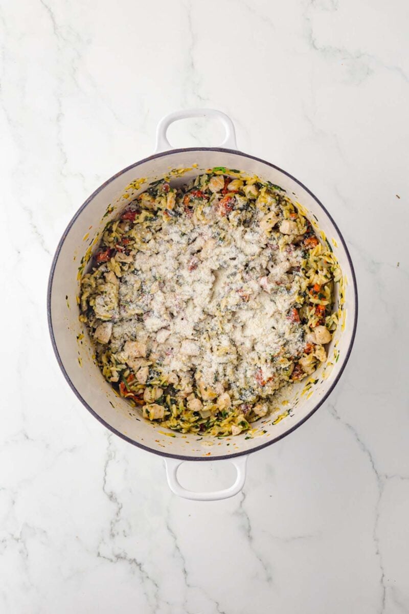 Parmesan cheese added to the top of tuscan chicken orzo in a dutch oven.
