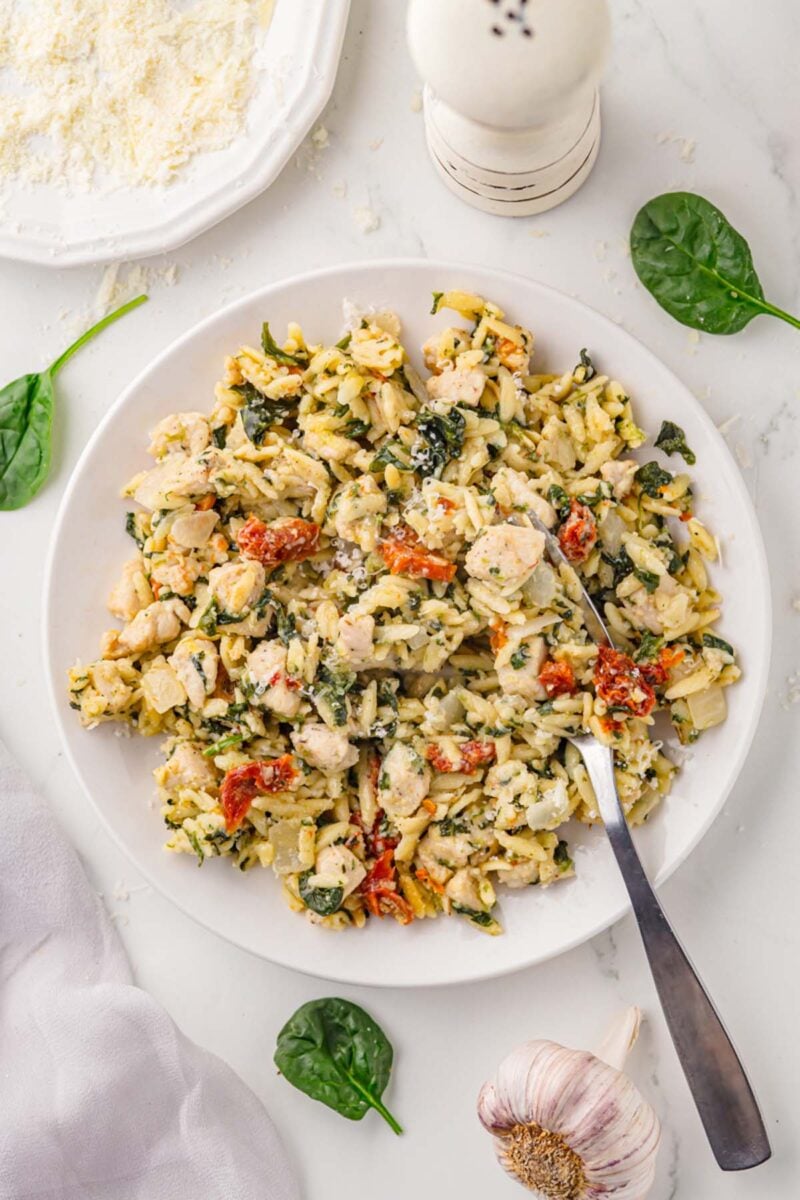 A serving of Tuscan Chicken Orzo on a white plate with a fork in it.