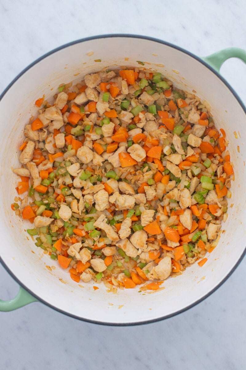 Celery, carrots, and onion added to cooked chicken in a dutch oven.