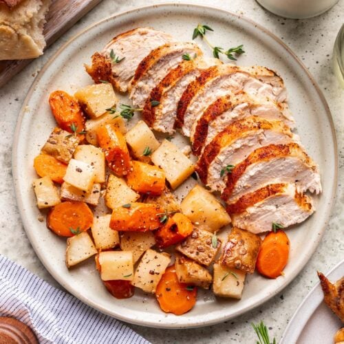 A plate with a sliced Dutch Oven Roast Chicken with carrots and potatoes on the side.