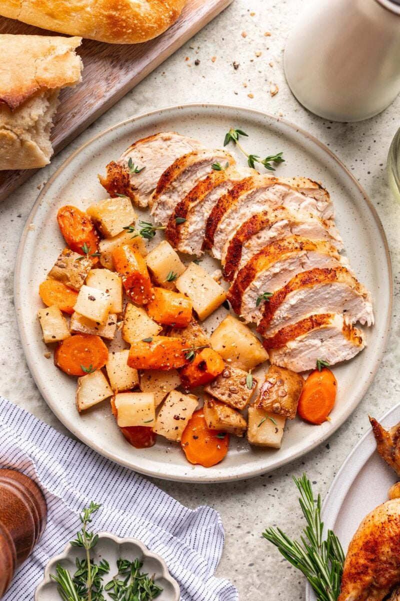 A plate with a sliced Dutch Oven Roast Chicken with carrots and potatoes on the side.