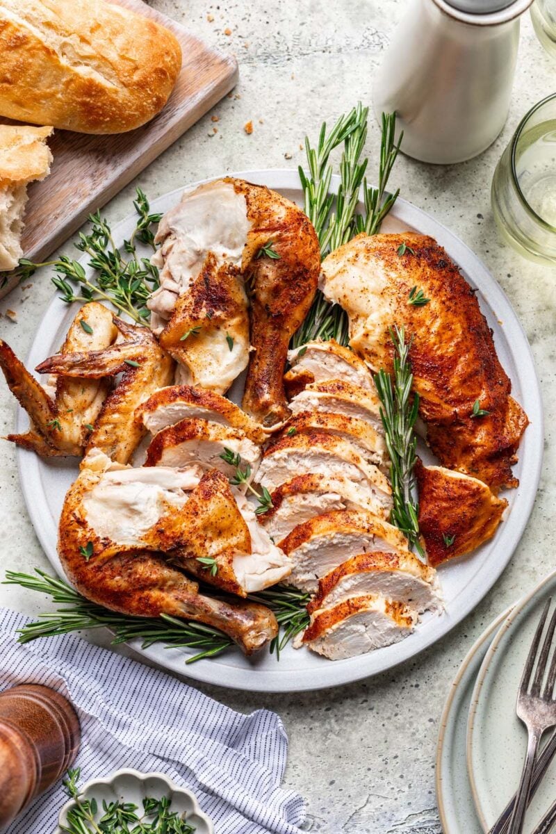 Sliced dutch oven whole chicken on a large plate with a piece of bread on the side.