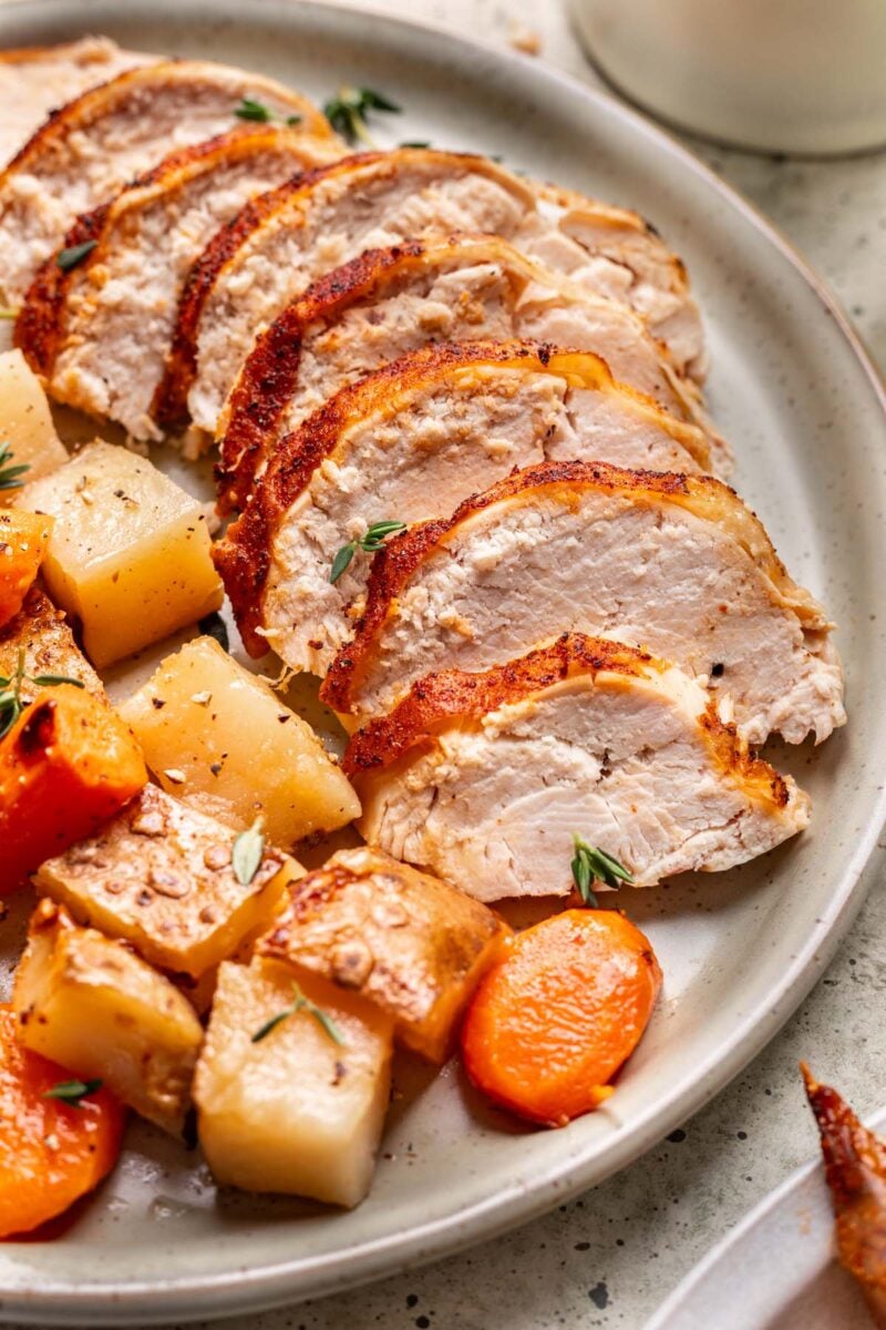 A close up of sliced dutch oven chicken on a plate with carrots and potatoes.