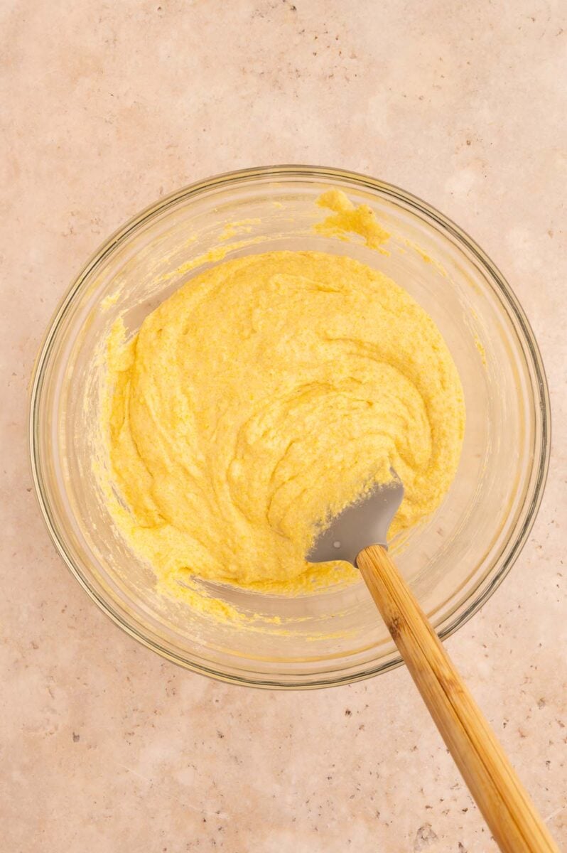 Healthy cornbread batter in a clear glass bowl with a spatula in it. 
