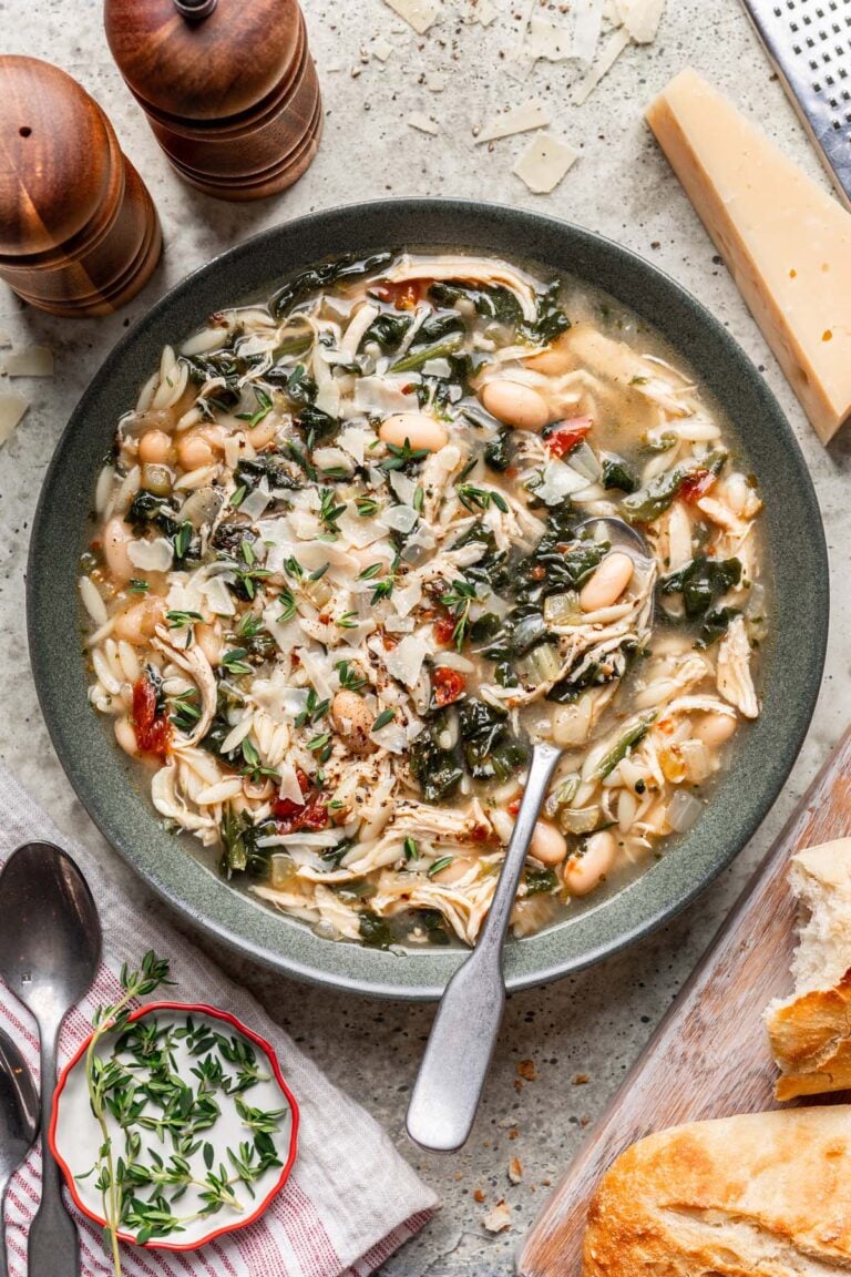 Tuscan Chicken Soup in a grey bowl with a spoon in it and parmesan cheese rind on the side.