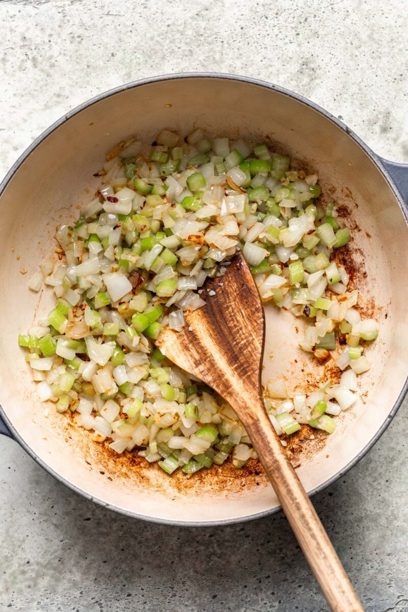 Celery and onion sauteing in a dutch oven with a wooden spoon in it.