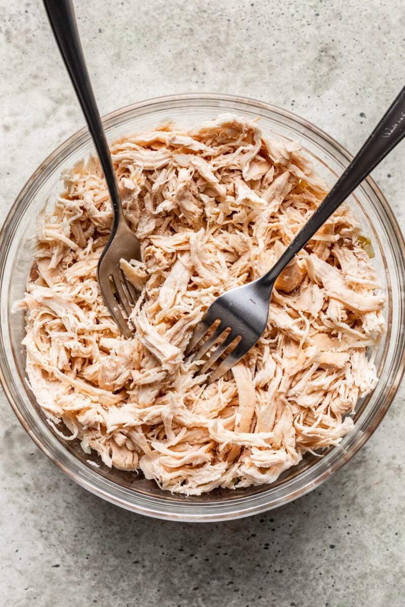 Two forks in a bowl shredding chicken.