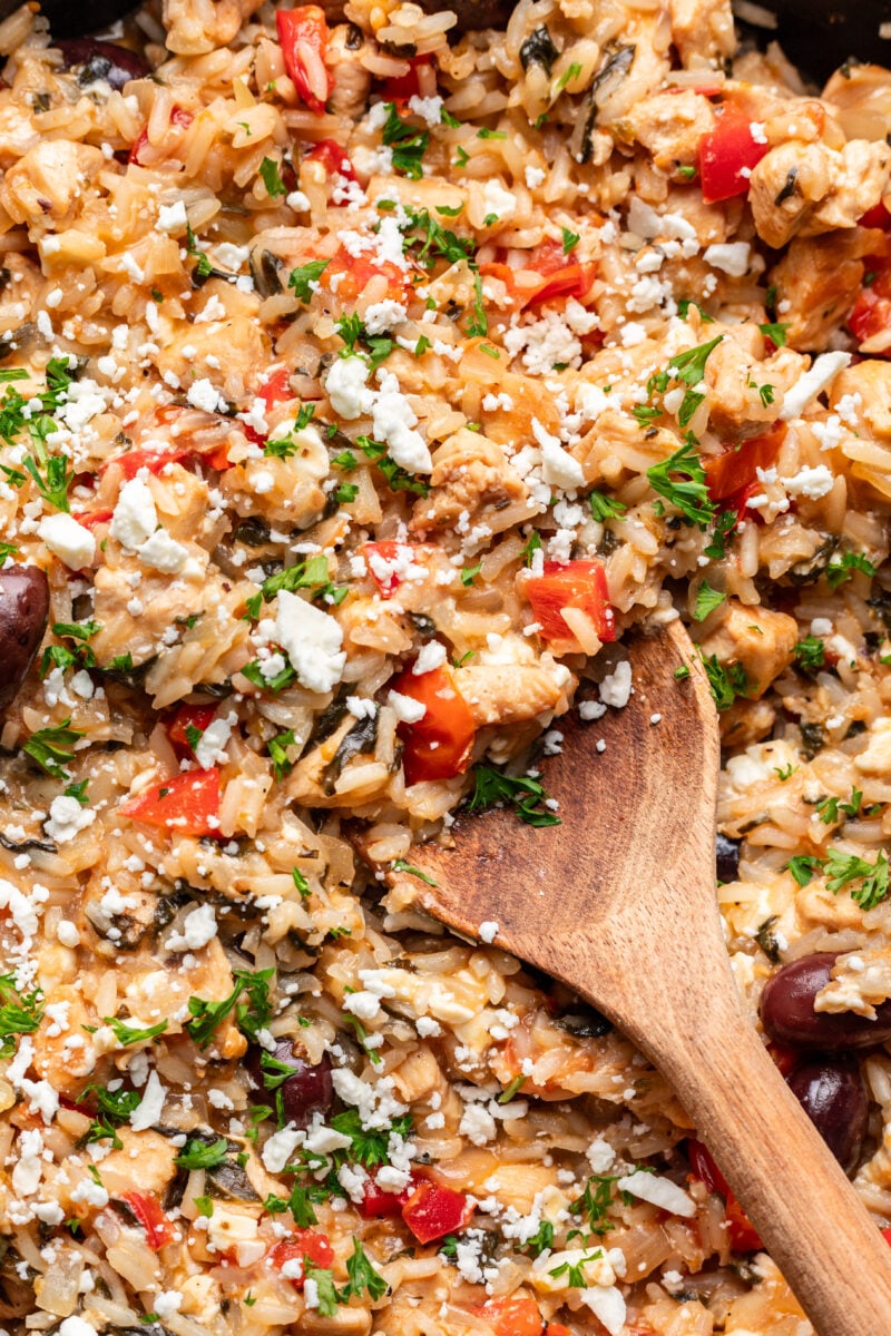 A close up of greek chicken and rice with a wooden spoon in it. 