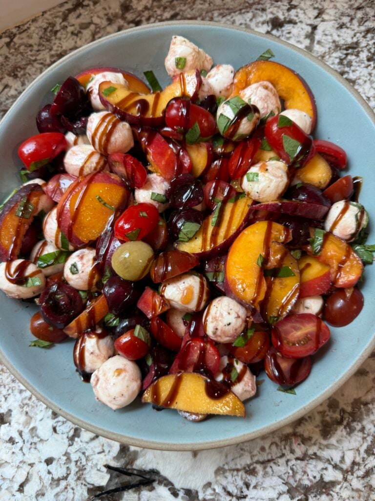 Peach Caprese Salad drizzled with balsamic glaze in a blue bowl